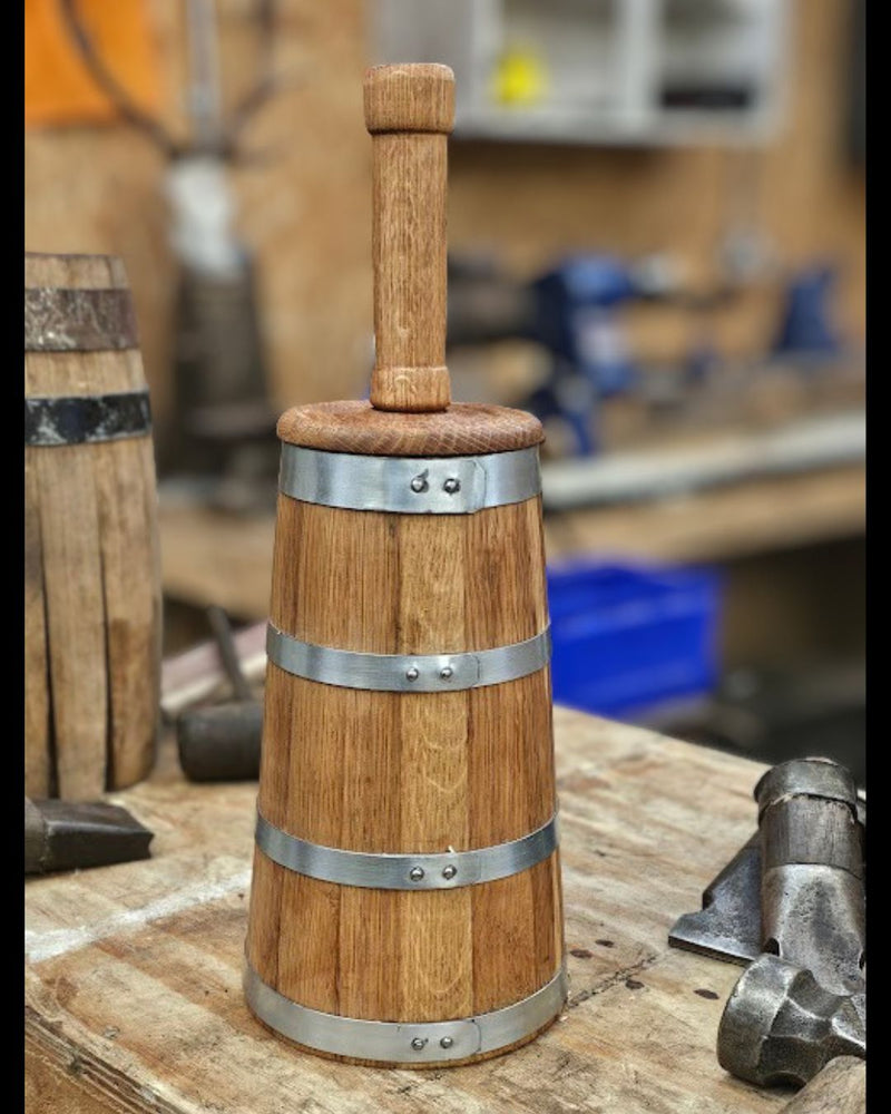 Small wooden oak coopered butter churn on workbench next to a barrel in progress and coopering tools. The background is out of focus.