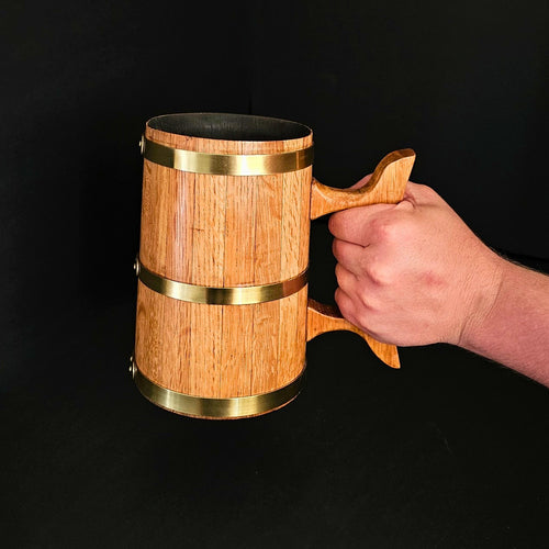 Wooden oak 1L Tankard with brass hoops, held by a hand on a black backdrop.