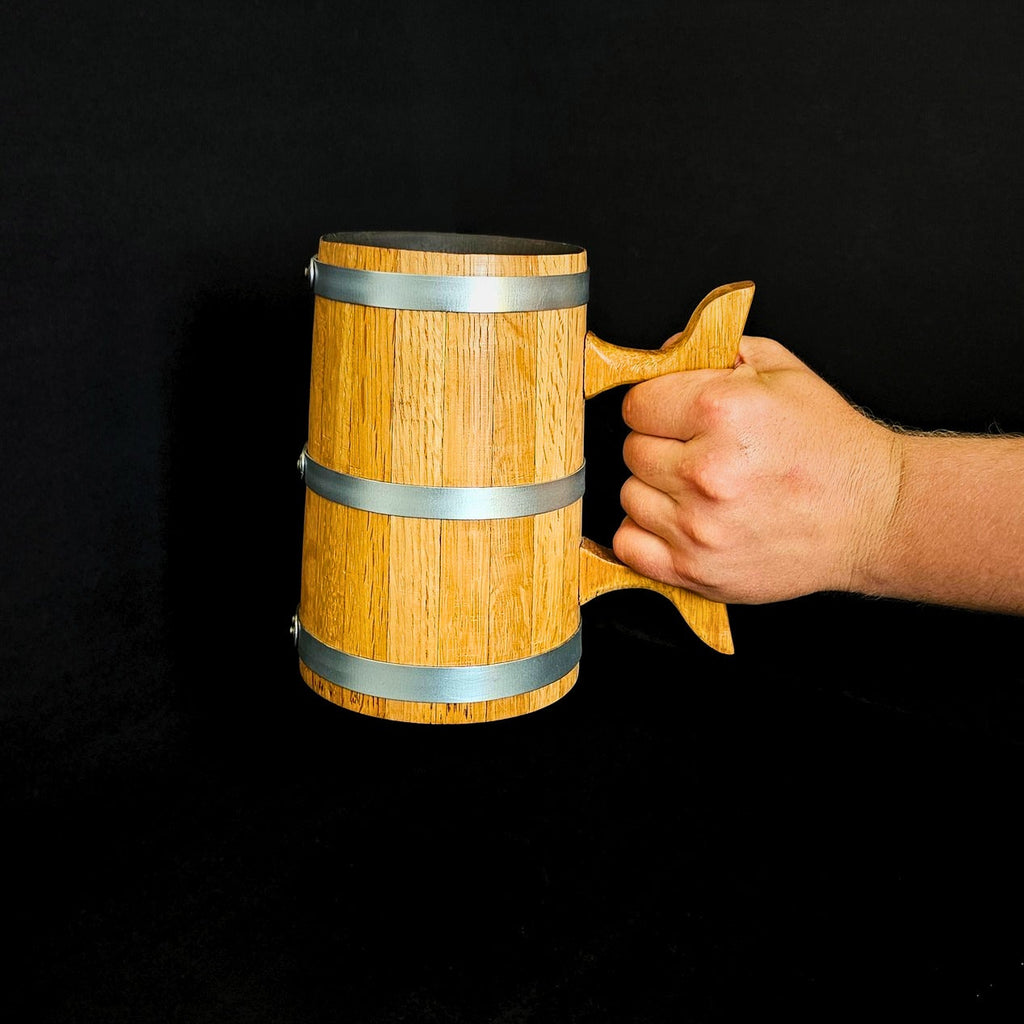 Wooden oak tankard with wooden handle and steel hoops held by hand on black background