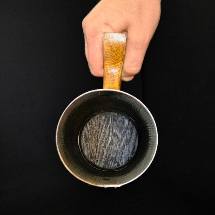 Wooden oak tankard with wooden handle and steel hoops and black background held by hand showing charred interior.